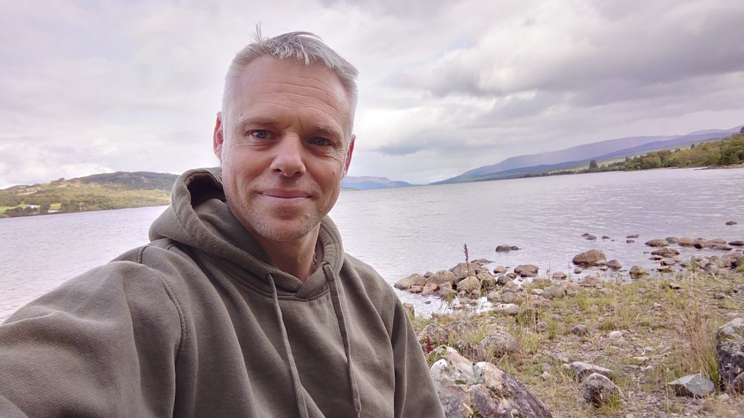 André De Warr beside a loch with mountains in the distance